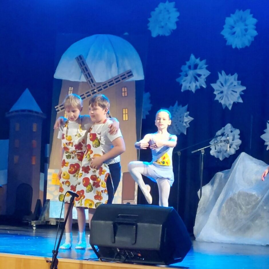 Divi zēni priekšautos un trīs meitenes baleta tērpos dejo uz skatuves