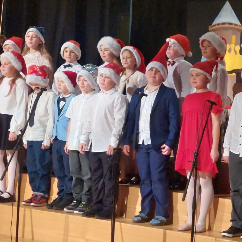 Bērni dzied uz skatuves, galvās rūķu cepures