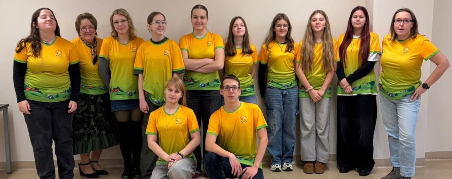 Skolēni un 2 skjolotājas demonstrē skolas jaunos T-kreklus: dzeltenzaļš fons un apakšā stilizēts Ropažu apkārtnes skats un skolas logo